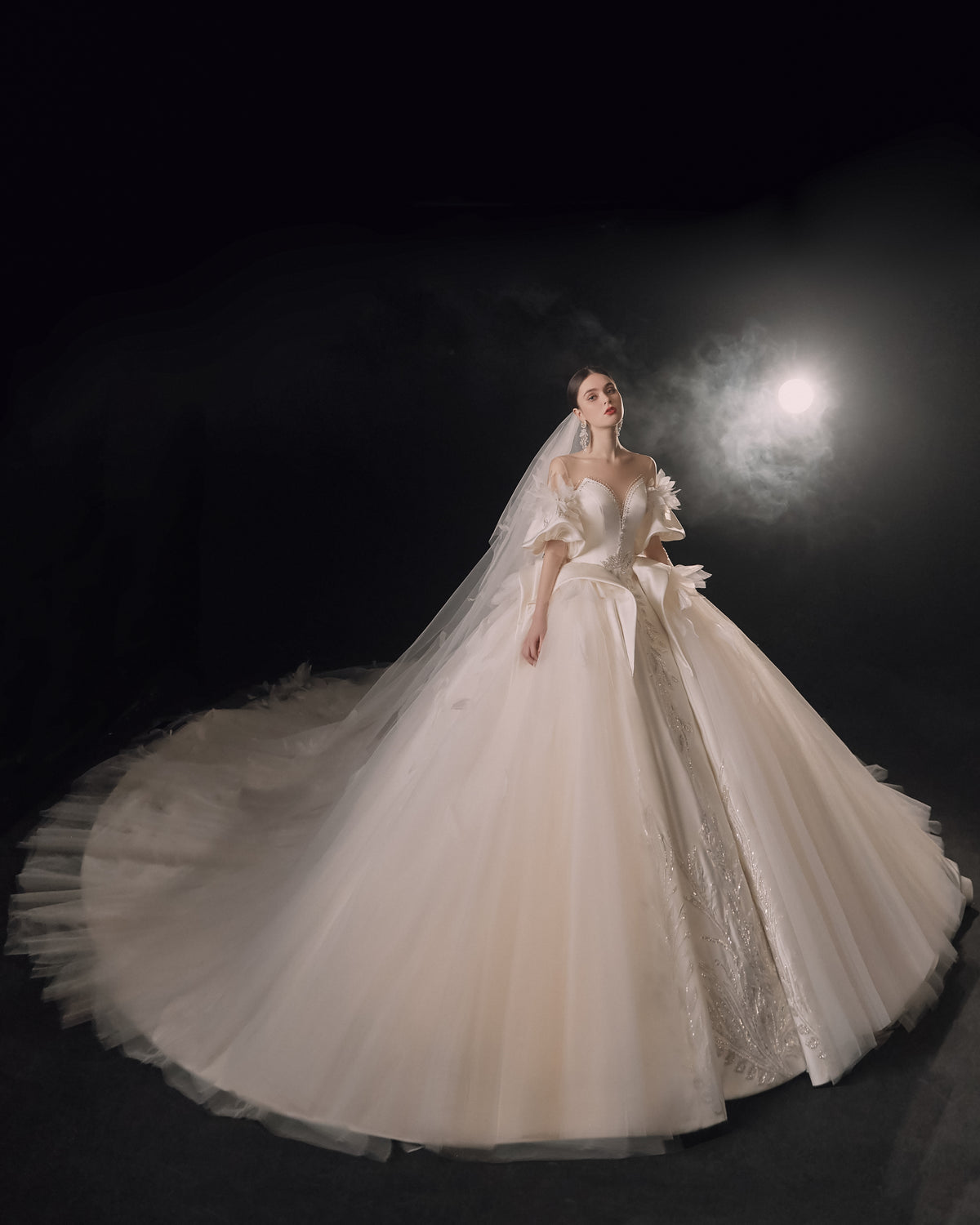 Abito da sposa etereo in raso con piume, scollatura a spalle scoperte, gonna ampia, strascico a cattedrale e dettagli in cristallo