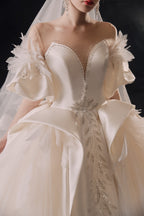 Abito da sposa etereo in raso con piume, scollatura a spalle scoperte, gonna ampia, strascico a cattedrale e dettagli in cristallo